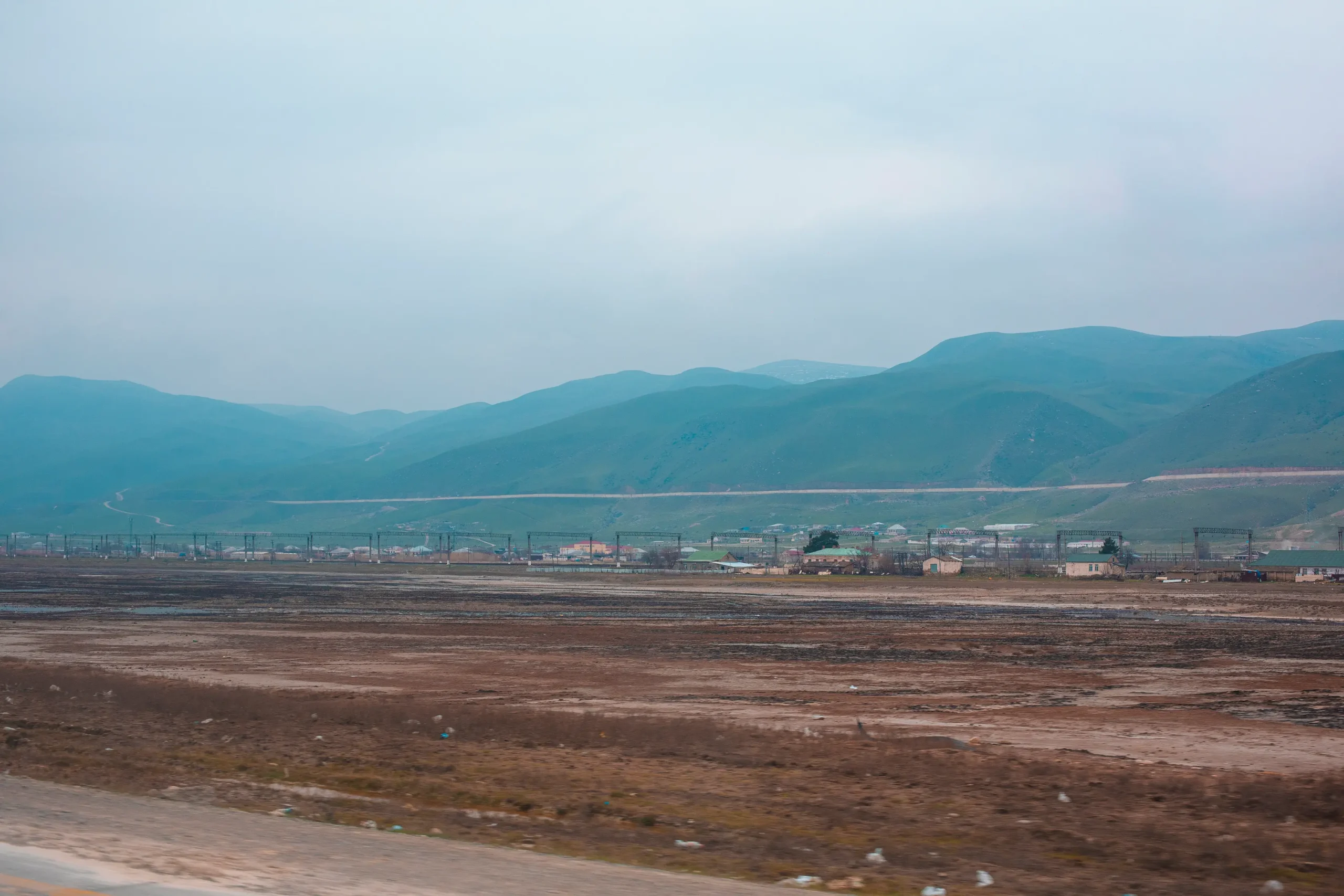 Foggy scenic roadside view of brown barren land, blue skies and green mountains in the background suited for land acquisition