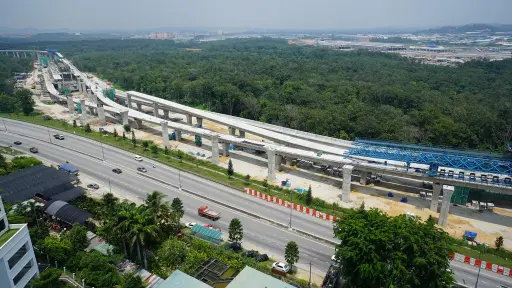 Birds view landscape image of Klang MRT project being constructed with a myriad of trees in the background, the construction site set beside a road littered with cars and some buildings at the front of the image