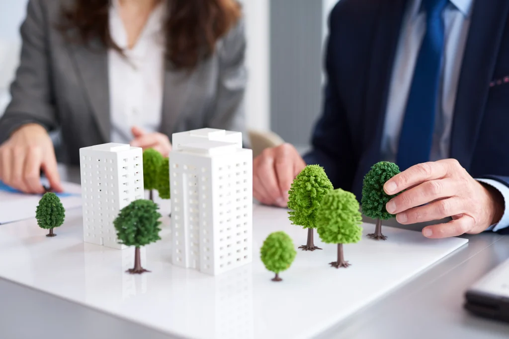 Merger and acquisition company in Malaysia professionals reviewing a property development model with miniature buildings and trees during a real estate planning discussion.