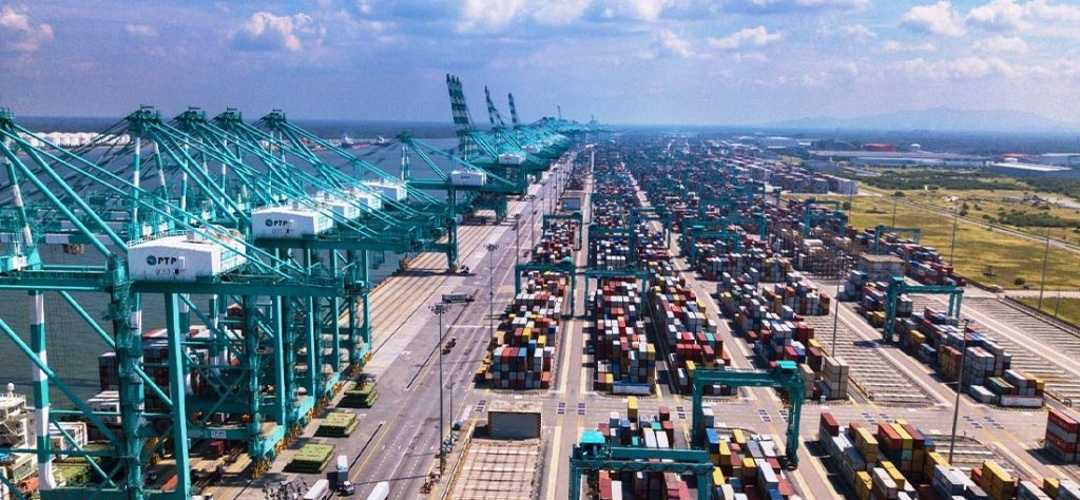 Industrial property and industrial property Klang Valley are reflected in this aerial photograph of Port Klang, showing a large-scale logistics and shipping hub filled with neatly stacked multicolored cargo containers, wide transport lanes, and towering teal gantry cranes aligned along the port. The scene captures active industrial operations with trucks moving through the container yard, emphasizing the scale, efficiency, and strategic importance of Klang Valley’s industrial infrastructure under a bright blue sky with scattered clouds.